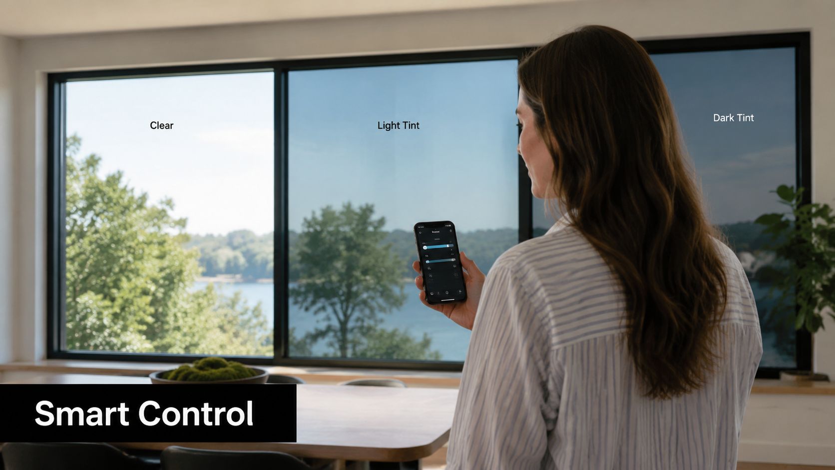 A woman using a smartphone to adjust smart window tints in a home with a scenic view.
